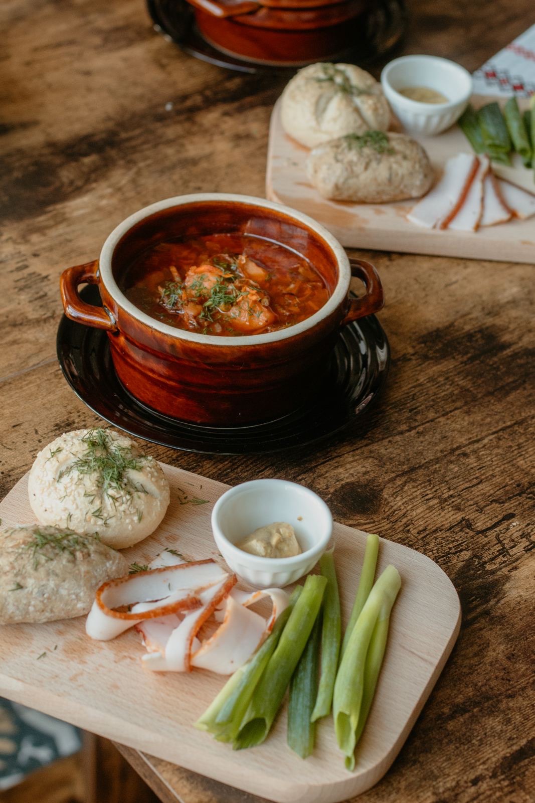 Tradycyjny obiad: czerwony barszcz w glinianej miseczce z uszkami, podany na drewnianym stole z pieczywem posypanym koperkiem, słoniną i zielonym szczypiorkiem na drewnianych deskach do krojenia.