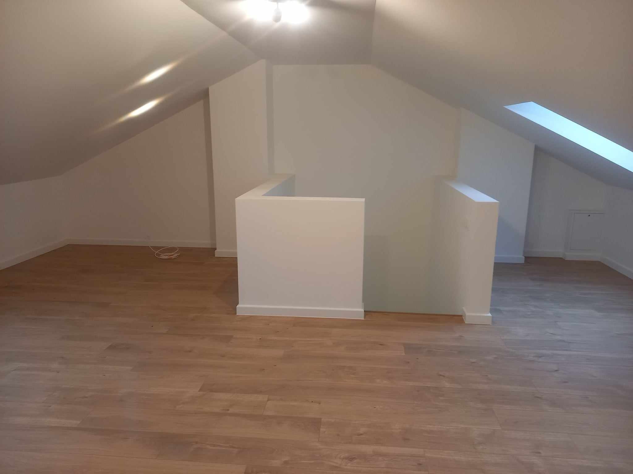 Poddasze po remoncie z jasnymi ścianami, drewnopodobną podłogą i oknem dachowym.