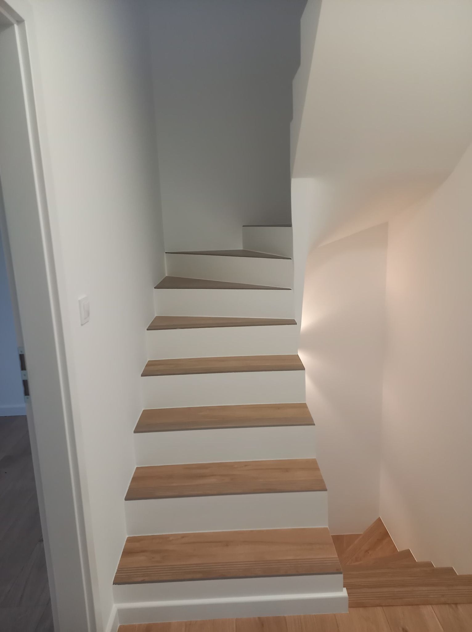 Białe schody z drewnianymi stopniami, widok z dołu na górę, minimalistyczny design, oświetlenie punktowe.