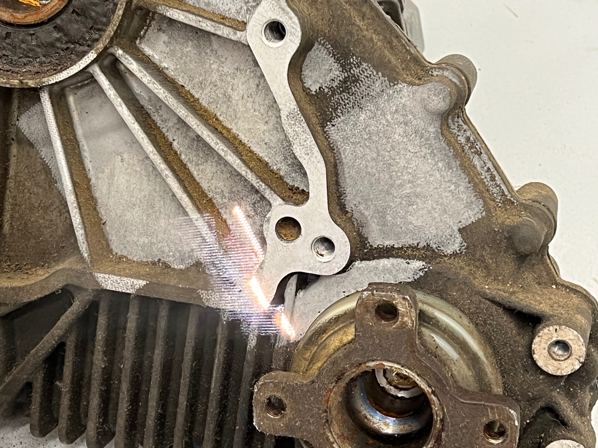 Fragment zdemontowanej, zabrudzonej skrzyni biegów z widocznymi elementami mocującymi i żebrowaniem chłodzącym.