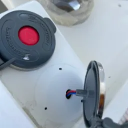 Montaż panelu sterowania z czerwonym przyciskiem i otwartą obudową z widocznymi przewodami na białej powierzchni.