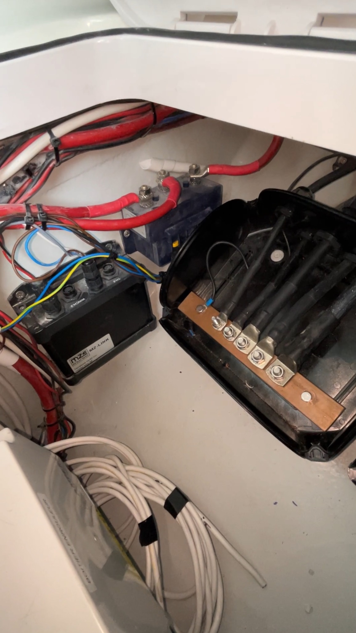 Skomplikowana instalacja elektryczna wewnątrz białej obudowy, widoczne kable w różnych kolorach, akumulator, moduł MZE MZ-LINK i skrzynka z grubymi przewodami zakończonymi metalowymi złączkami.