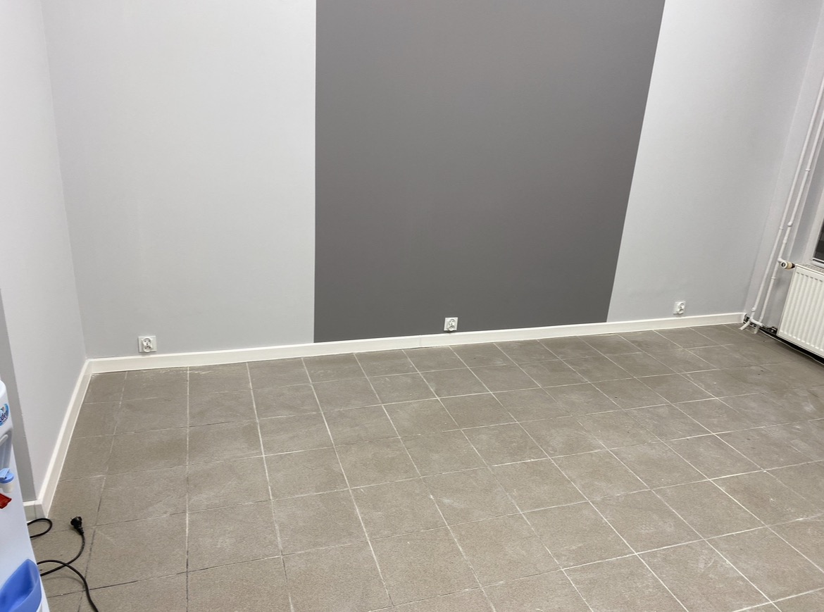 Pusty pokój z szarą i białą ścianą, szarą podłogą z płytek i gniazdkami elektrycznymi na ścianach.