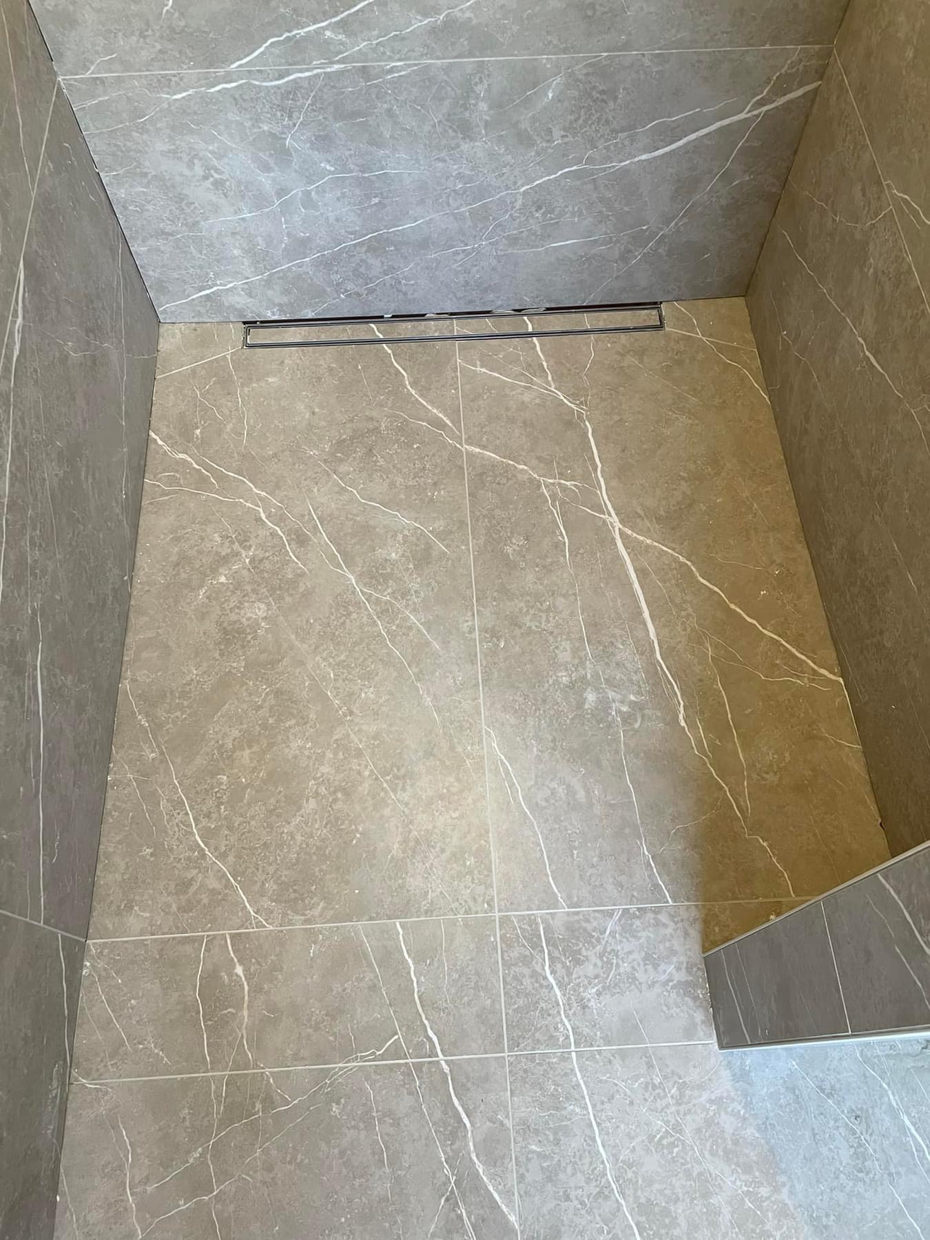 Kabina prysznicowa wyłożona szarymi płytkami imitującymi marmur z odpływem liniowym w podłodze.