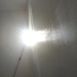 Quality House - Świeżo pomalowana ściana z widocznym wałkiem malarskim i intensywnym odbiciem światła, ukazująca teksturę farby.