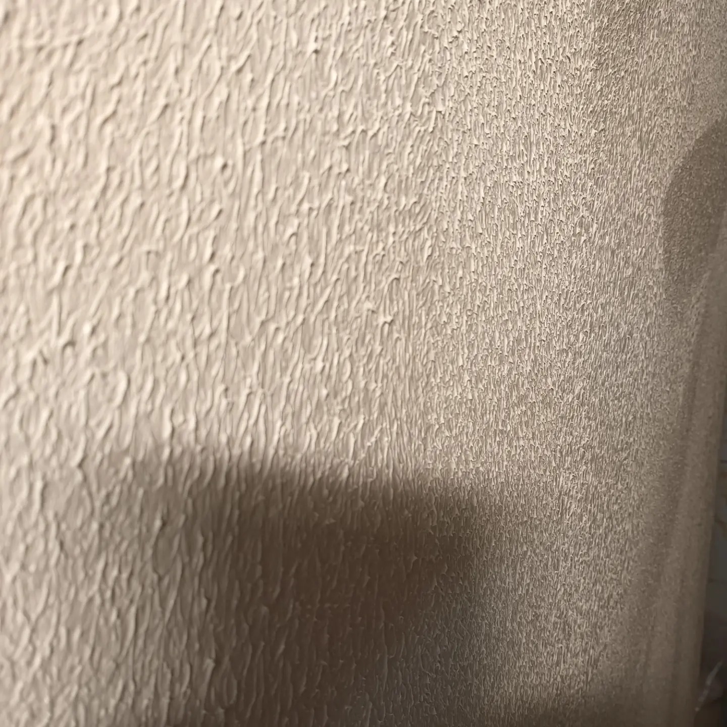 Tekstura ściany pokrytej jasną, strukturalną farbą, z widocznym cieniem po prawej stronie.