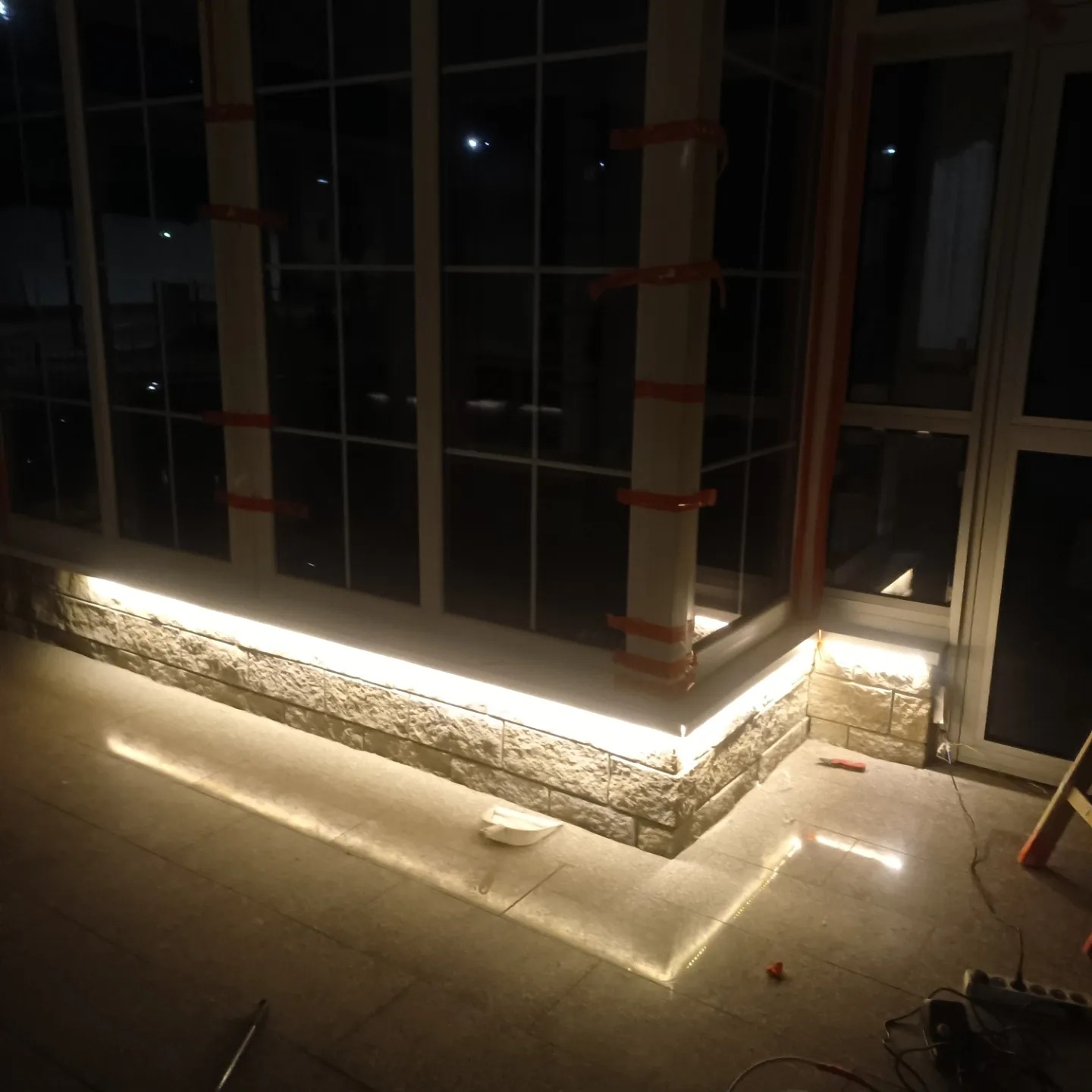 Oświetlenie LED zamontowane wzdłuż okna i murku, z widocznymi przewodami i narzędziami na podłodze, sugerujące etap instalacji.
