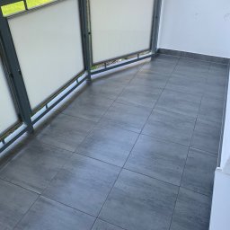 Rafbud - Wykończony balkon z szarymi płytkami podłogowymi, metalową balustradą z wypełnieniem z tworzywa sztucznego i widokiem na zieleń.