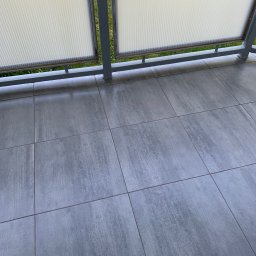 Rafbud - Szare, kwadratowe płytki gresowe na balkonie, widok z góry, z fragmentem balustrady z wypełnieniem z tworzywa sztucznego.