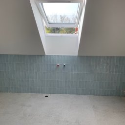 Rafbud - Świeżo położone, pionowe, błękitne płytki w łazience na poddaszu z oknem dachowym i przygotowanymi wyprowadzeniami na baterie oraz odpływem w podłodze.