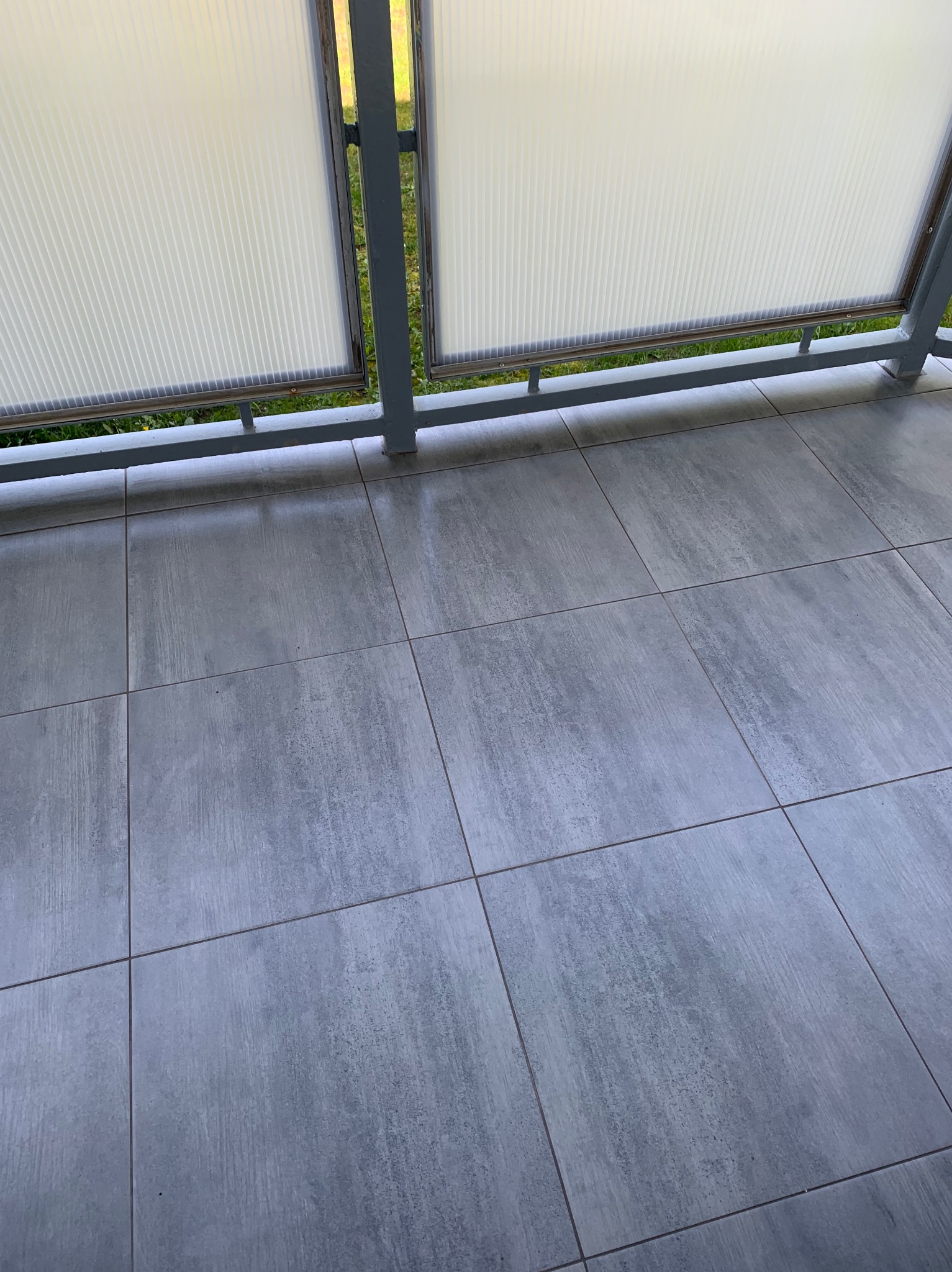 Szare, kwadratowe płytki gresowe na balkonie, widok z góry, z fragmentem balustrady z wypełnieniem z tworzywa sztucznego.