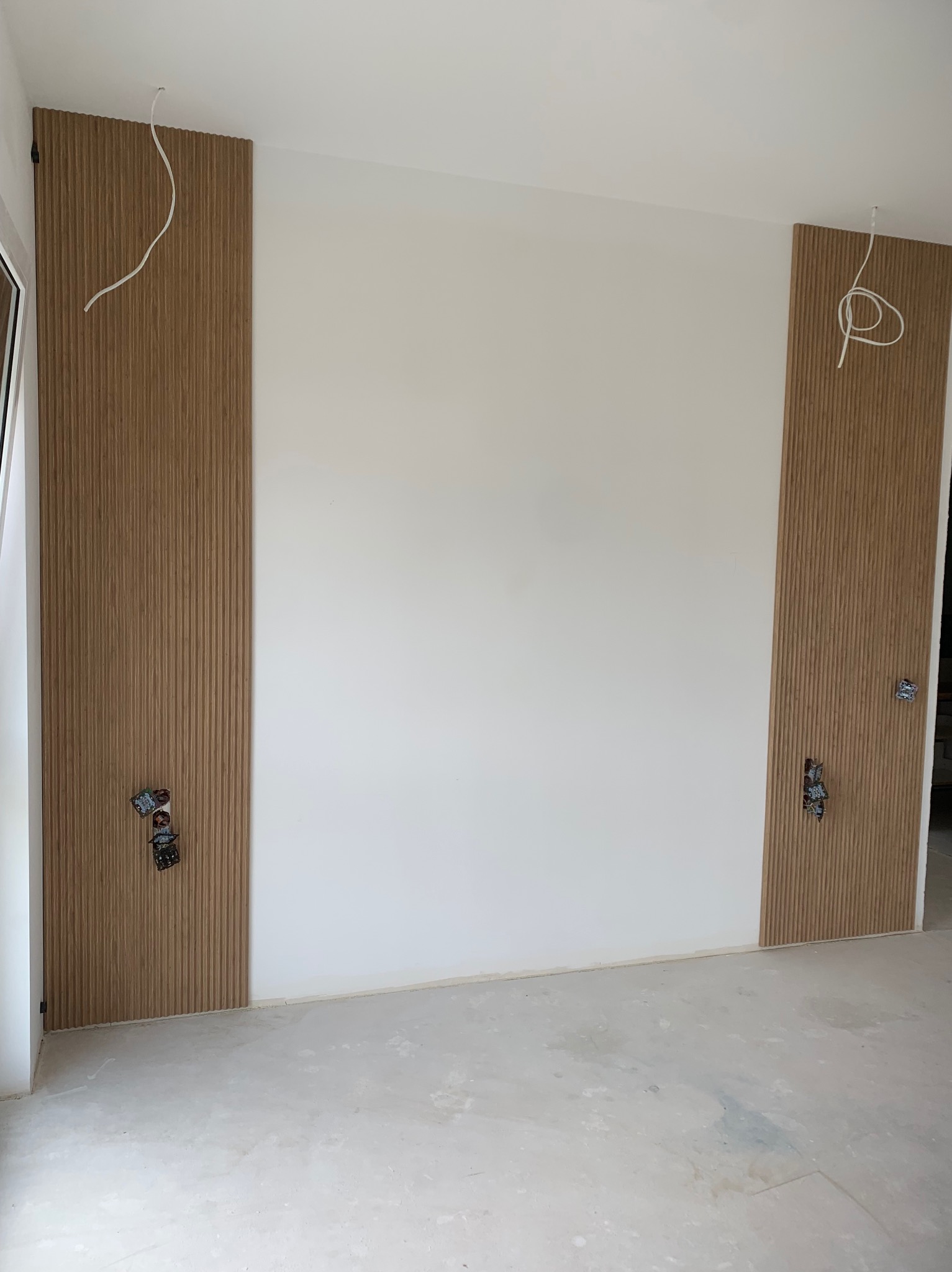 Montaż drewnianych paneli ściennych z widocznymi puszkami elektrycznymi i wystającymi przewodami w pomieszczeniu w trakcie wykańczania.