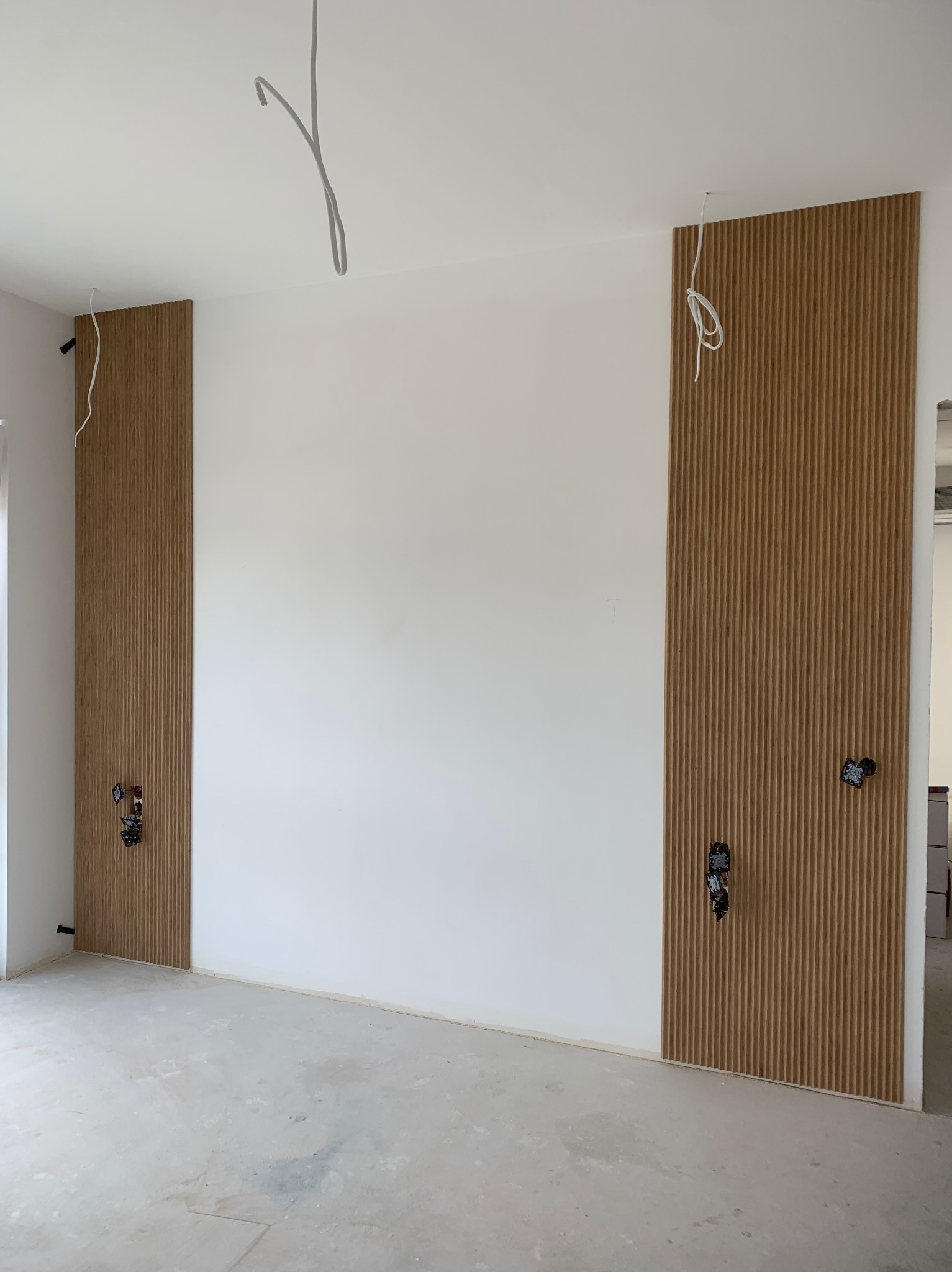 Montaż dekoracyjnych paneli ściennych z drewna w Bydgoszczy, widoczne wystające przewody elektryczne i surowy beton na podłodze.