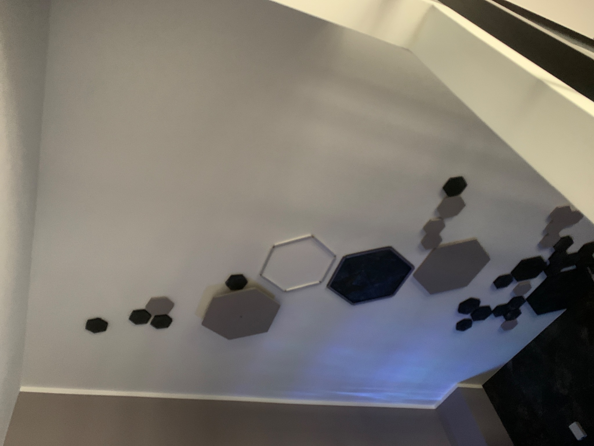 Aranżacja ściany z sześciokątnych paneli akustycznych w różnych odcieniach szarości i czerni, tworzących geometryczny wzór na jasnej ścianie.