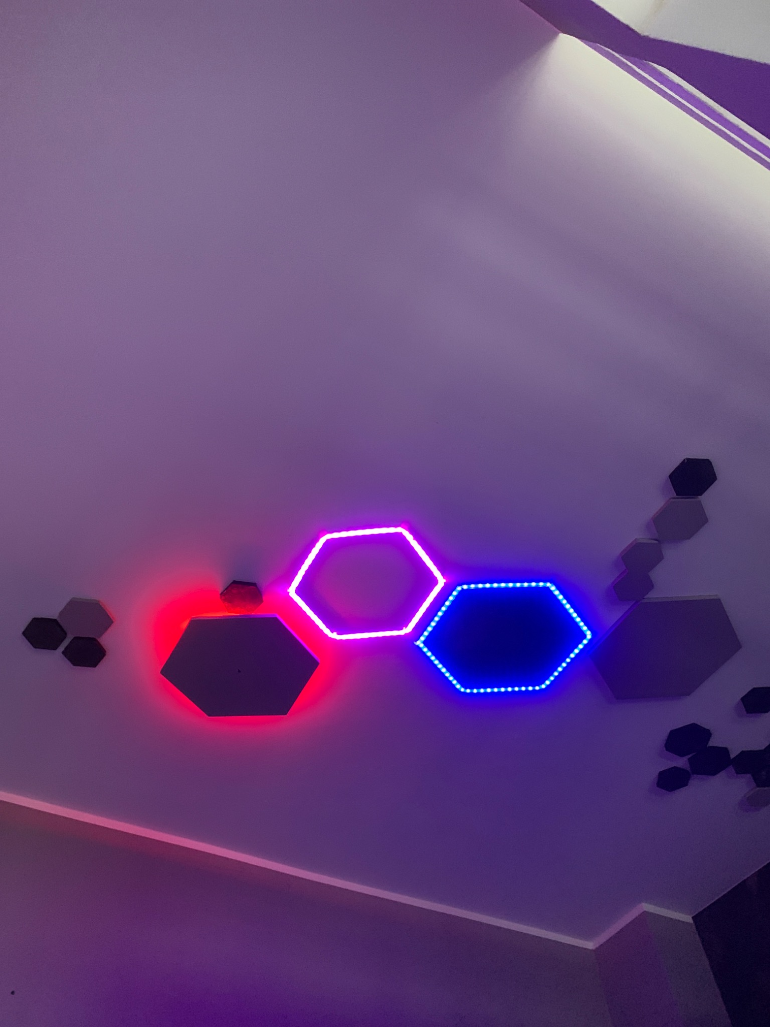 Sufit z dekoracyjnymi panelami LED w kształcie sześciokątów, świecących na czerwono, różowo i niebiesko, oraz dodatkowymi panelami w kolorze szarym i czarnym.