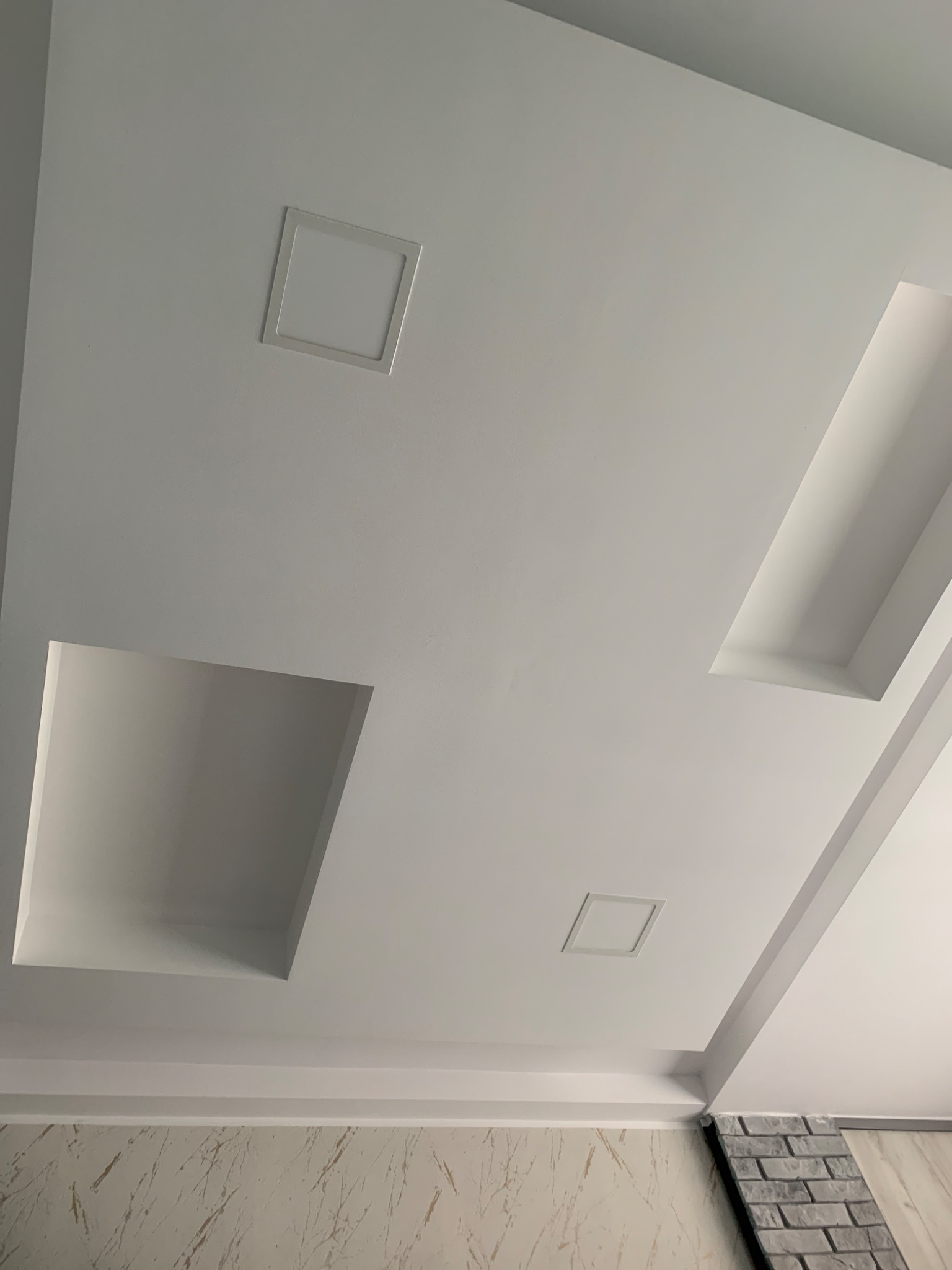 Biały sufit podwieszany z oświetleniem LED i dekoracyjnymi wnękami w Bydgoszczy, widok z dołu, fragment ściany z imitacją cegły.