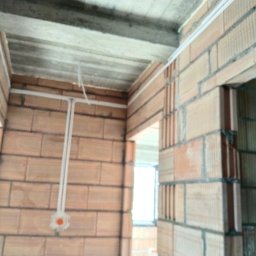 Jakub Ogar - Wewnętrzne ściany z cegły w surowym stanie w Nowym Sączu z widocznymi przewodami elektrycznymi i puszką instalacyjną podtynkową.