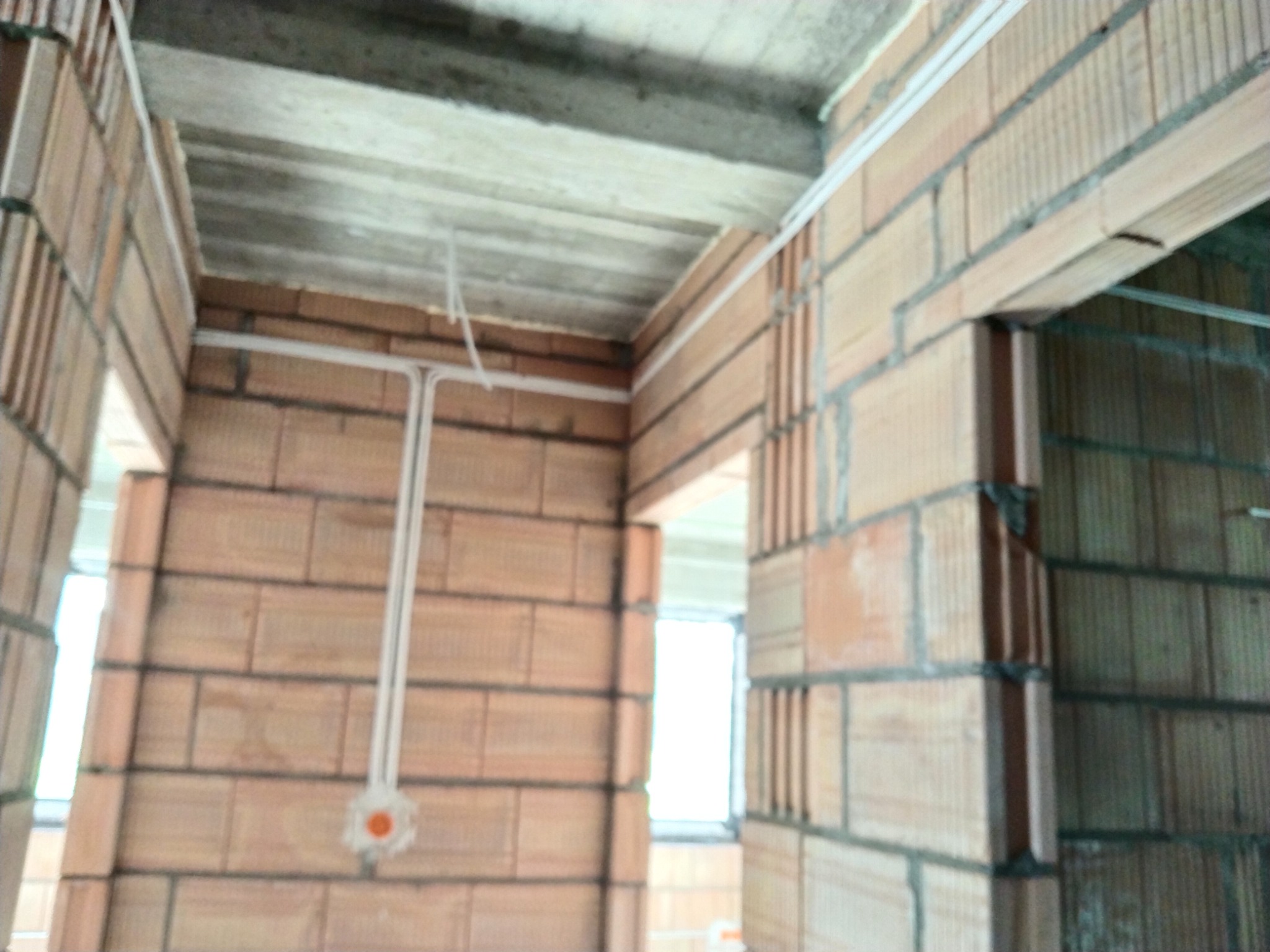 Wewnętrzne ściany z cegły w surowym stanie w Nowym Sączu z widocznymi przewodami elektrycznymi i puszką instalacyjną podtynkową.