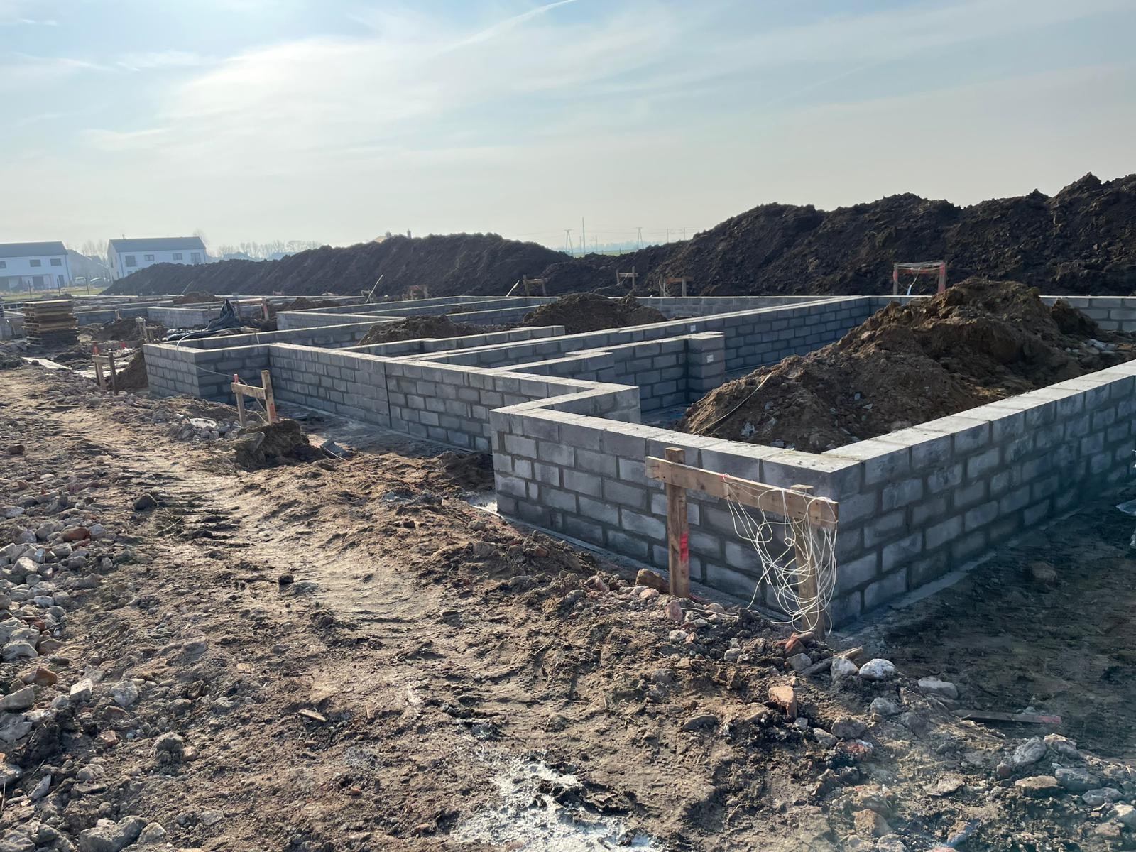 Fundamenty domu z bloczków betonowych, widoczne z ziemi, z hałdami ziemi w tle. Świeża konstrukcja w surowym stanie, przygotowana do dalszych prac budowlanych.