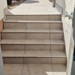 Jasne, płytki ceramiczne ułożone na schodach zewnętrznych prowadzących na taras, widoczne krzyżyki dystansowe w fugach.