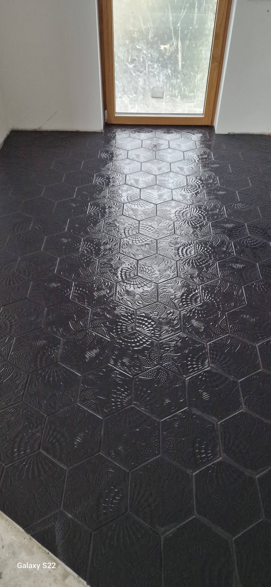 Ułożona, błyszcząca, heksagonalna, czarna podłoga z wzorem, w pobliżu okna połaciowego.