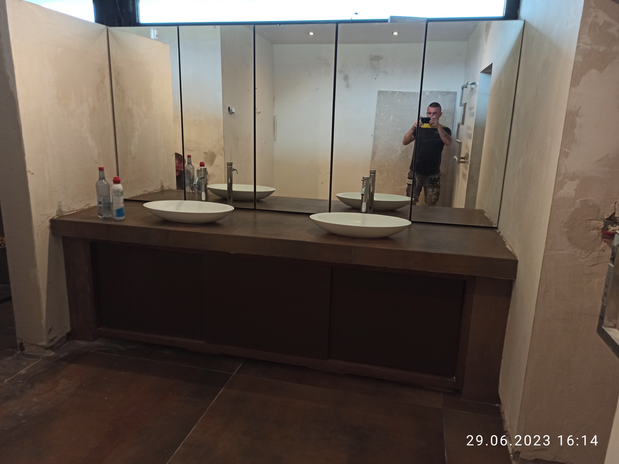 Łazienka w trakcie remontu: zamontowane umywalki nablatowe, lustra z czarnymi ramami, ściany w stanie surowym przed malowaniem, widoczny pracownik robiący zdjęcie.