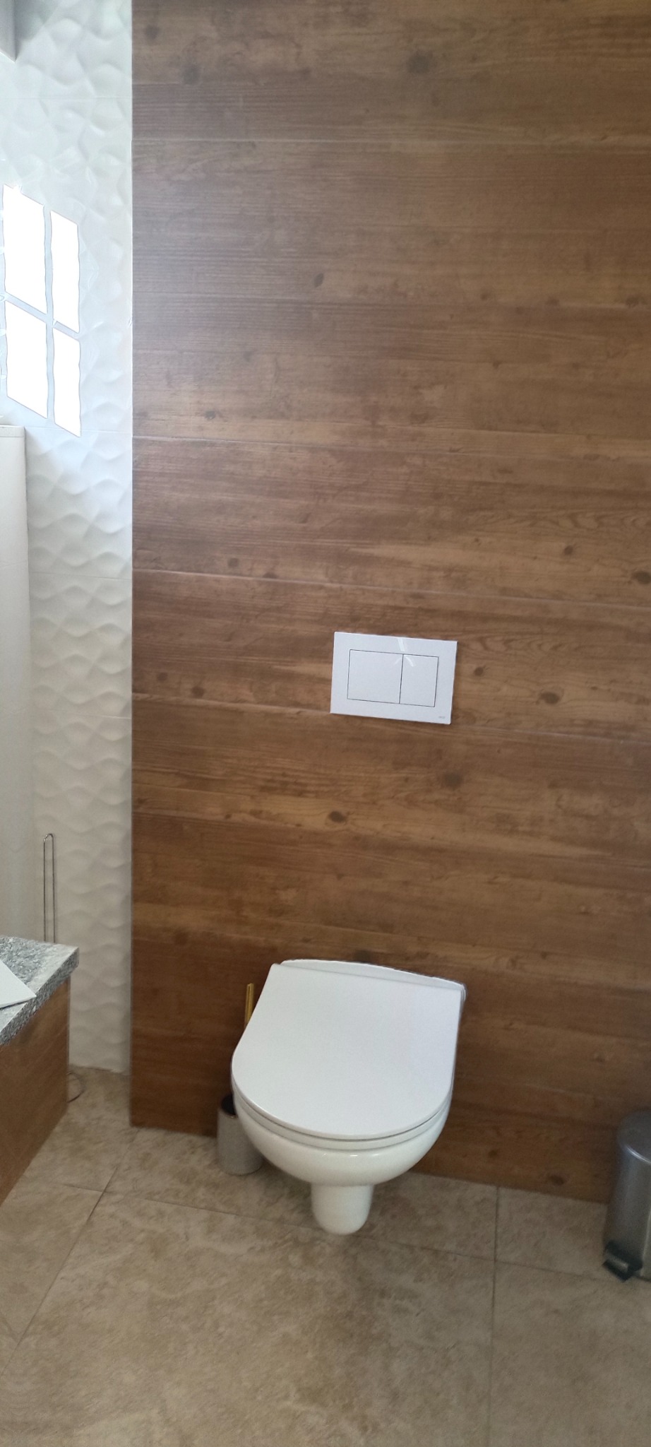 Nowoczesna toaleta z podwieszanym stelażem i drewnopodobną okładziną ścienną w łazience w Dąbrowie Górniczej, widoczne białe płytki strukturalne i szara podłoga.