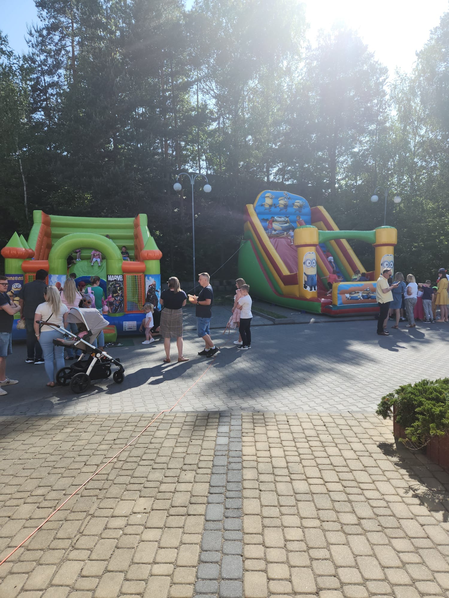 Dwa dmuchane zamki, jeden z motywem Marvela, drugi z Minionkami, otoczone grupą ludzi na imprezie plenerowej.