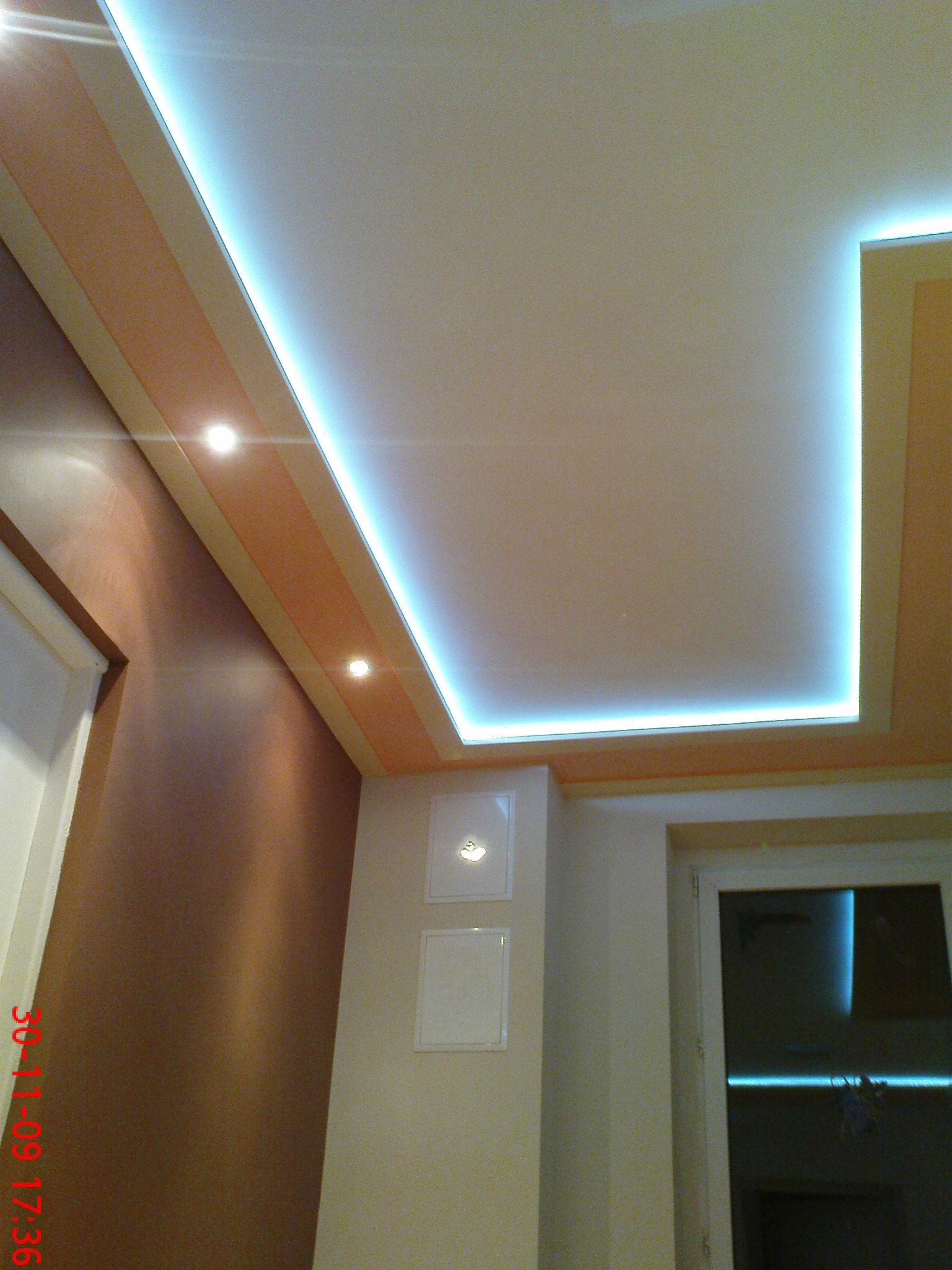 Podwieszany sufit z oświetleniem LED wzdłuż krawędzi, z dwoma punktowymi lampami i dekoracyjnym pasem na ścianie.