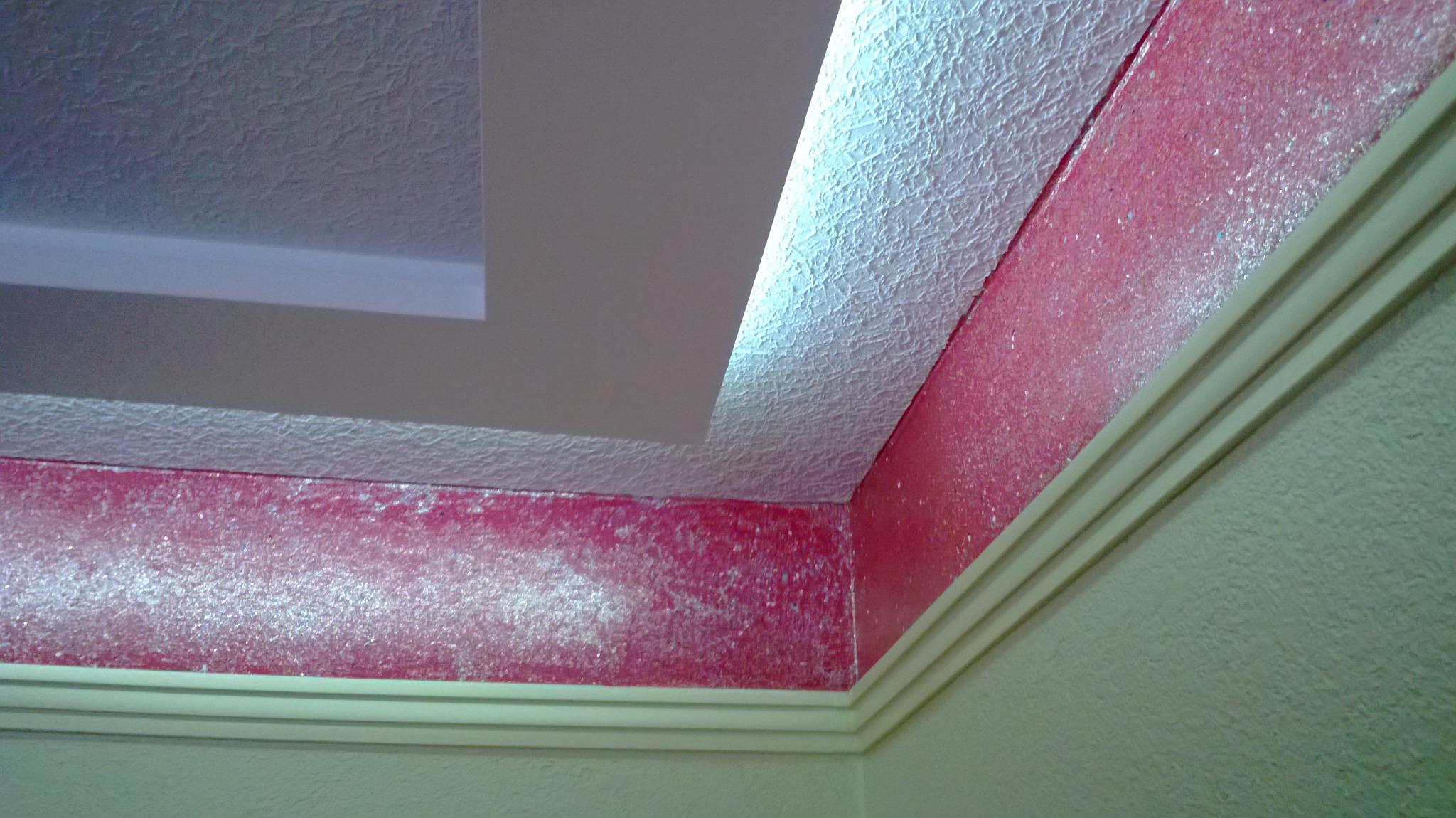 Fragment rogu pokoju: strukturalny sufit z wnęką, ściana pomalowana na różowo z efektem brokatu, dekoracyjny gzyms.