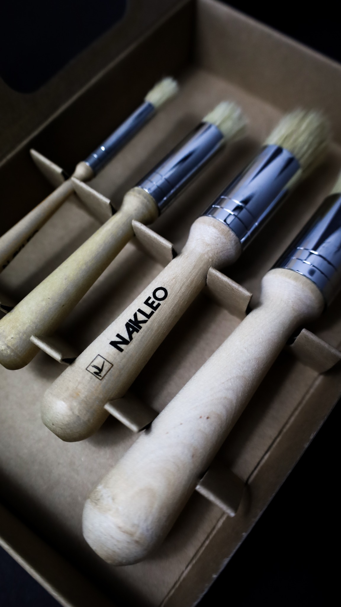 Zestaw czterech pędzli malarskich marki NAKLEO z drewnianymi rączkami i metalowymi skuwkami, ułożonych w tekturowym pudełku.