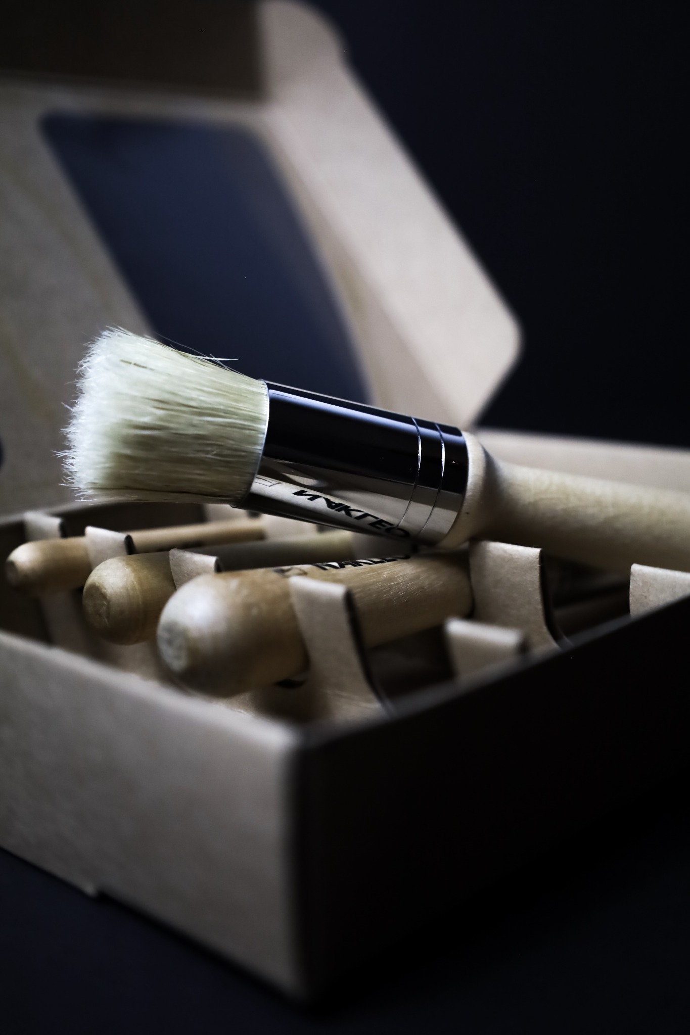 Zestaw pędzli z jasnym włosiem i drewnianą rączką w kartonowym pudełku z przegródkami, widoczne logo producenta na metalowej obręczy.