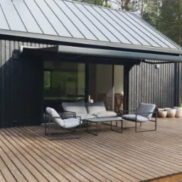 Nowoczesny dom z czarną drewnianą elewacją, szarą metalową konstrukcją nad tarasem i drewnianym tarasem z szarymi meblami wypoczynkowymi.