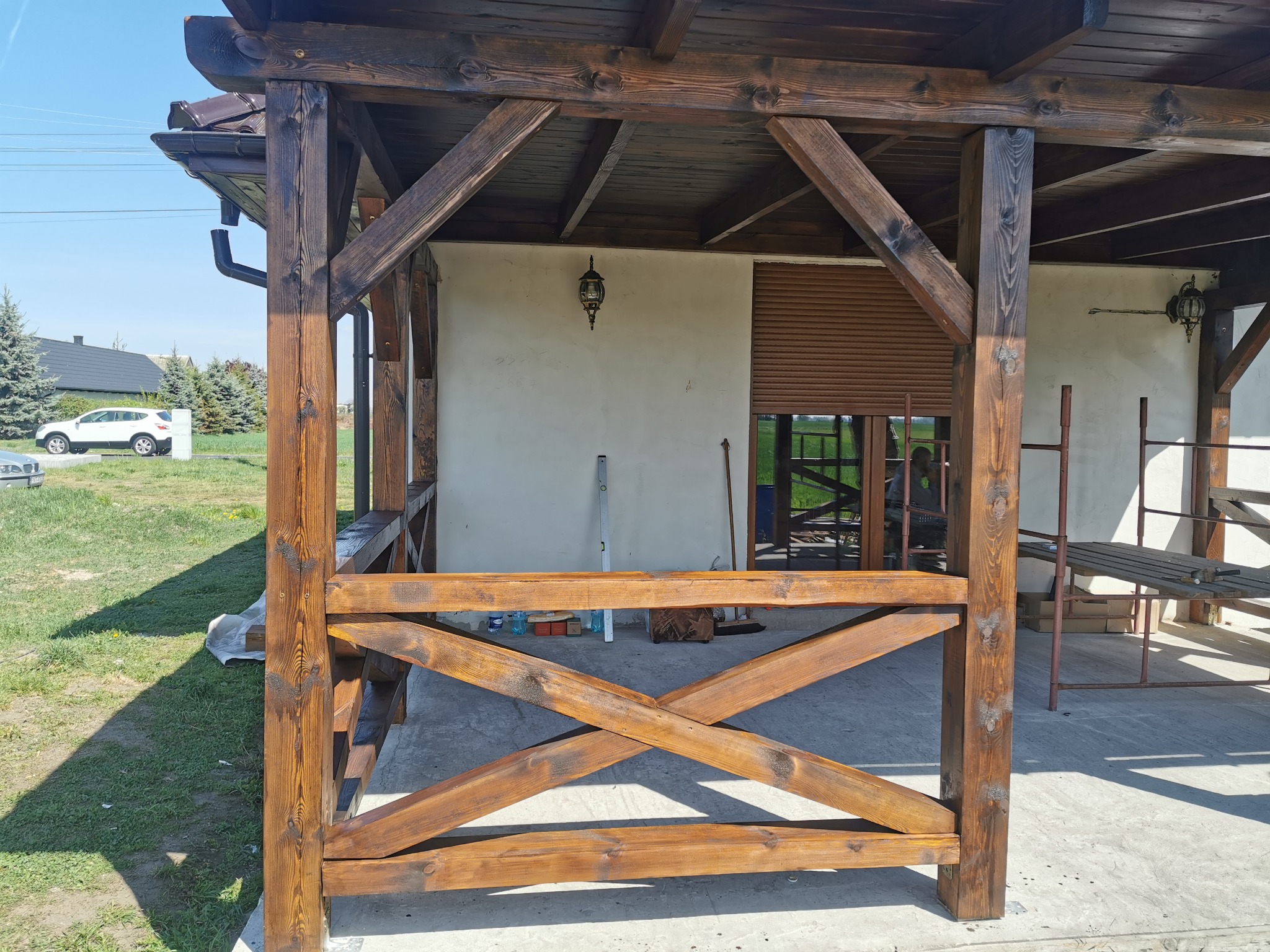 Drewniana konstrukcja z elementami zadaszenia i rynną widoczna w słoneczny dzień, z widoczną strukturą drewna i elementami wykończeniowymi.