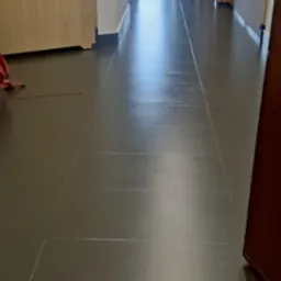 Ułożona, ciemnoszara podłoga z paneli w korytarzu z widoczną fugą, z fragmentem drzwi po prawej stronie i widokiem na dalszą część mieszkania w tle.