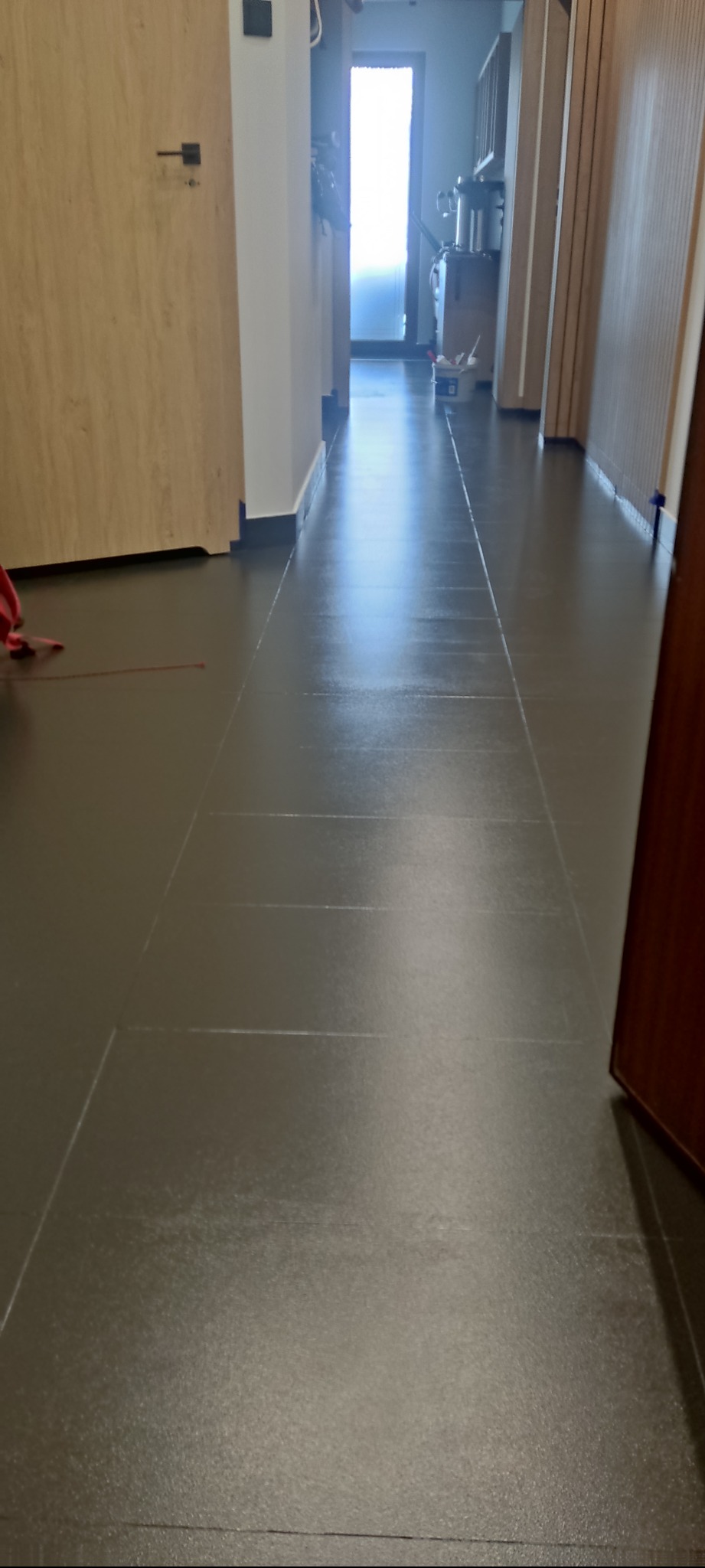 Ułożona, ciemnoszara podłoga z paneli w korytarzu z widoczną fugą, z fragmentem drzwi po prawej stronie i widokiem na dalszą część mieszkania w tle.