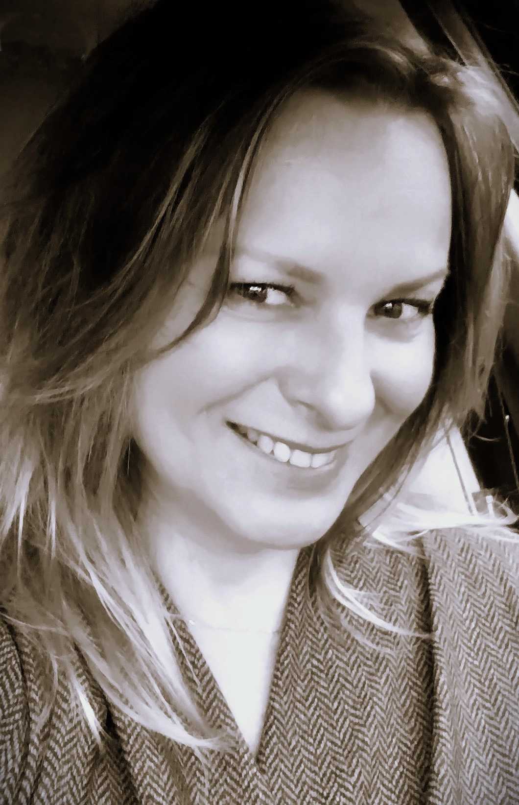 Portret uśmiechniętej kobiety w tweedowej marynarce, wykonany w sepii, z widocznymi zmarszczkami mimicznymi wokół oczu.