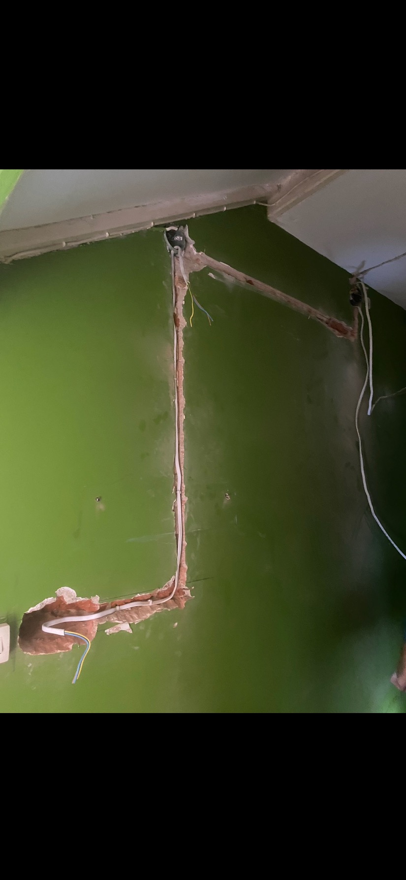 Zielona ściana z wyżłobionymi bruzdami pod kable elektryczne. Widoczne przewody w ścianie i puszki elektryczne. Etap prac instalacyjnych.