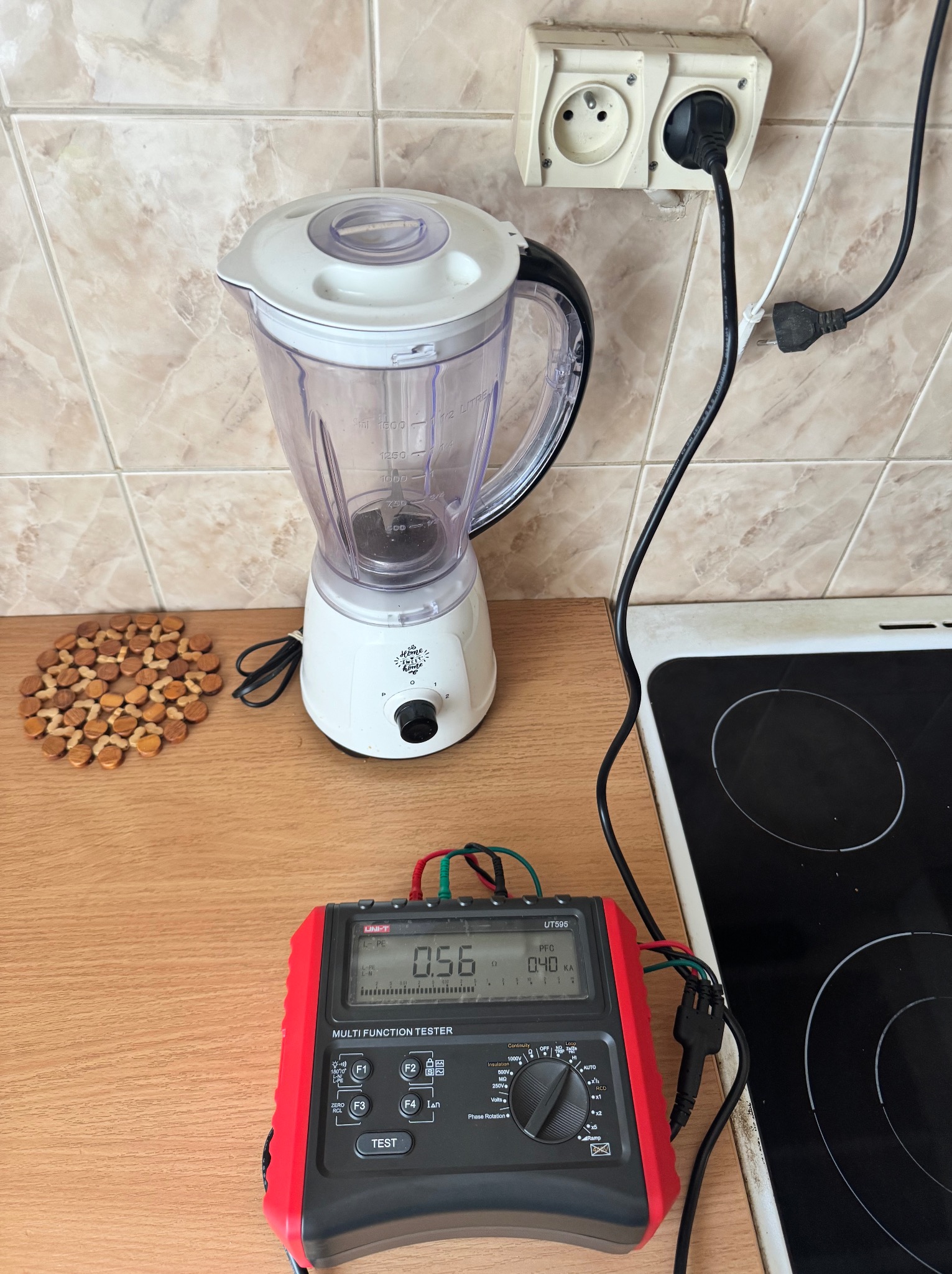 Pomiar parametrów elektrycznych gniazdka w kuchni za pomocą miernika wielofunkcyjnego Uni-T UT595. Widoczny blender i płyta indukcyjna. Diagnostyka instalacji.