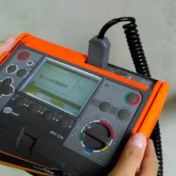 Pomiar napięcia w gniazdku elektrycznym za pomocą miernika Sonel MPI-520; wyświetlacz pokazuje wartość 230.5V.