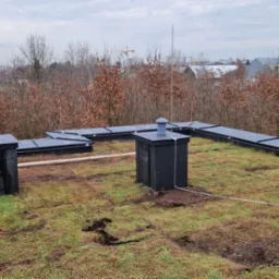 Instalacja odgromowa na zielonym dachu budynku w Wolbromiu, widoczne przewody i elementy systemu odgromowego, tło stanowią drzewa i zabudowa miejska.