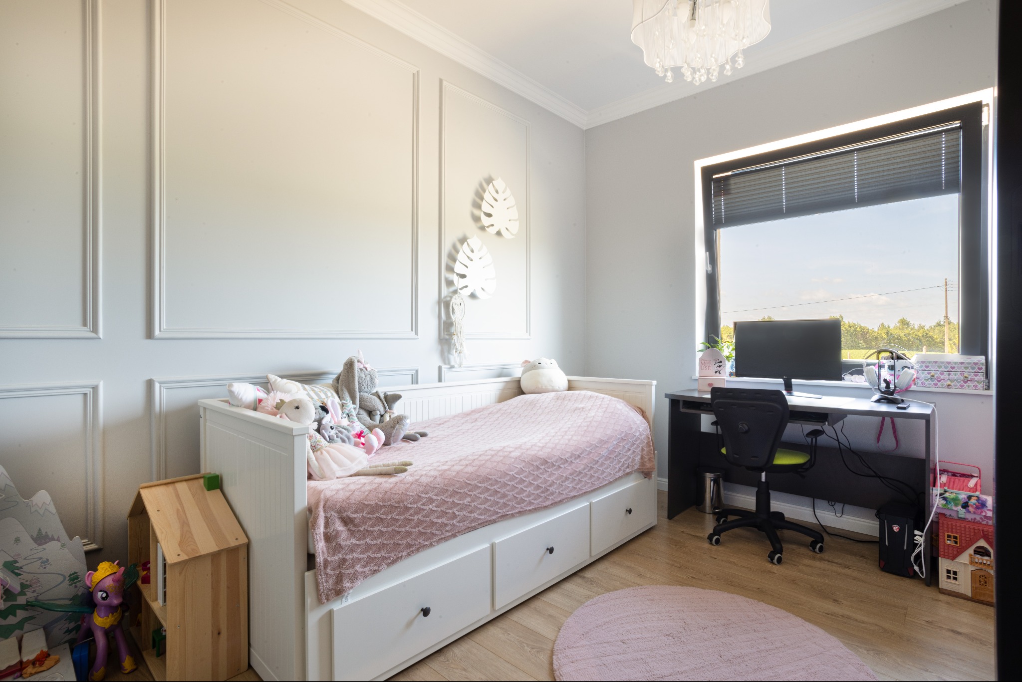 Pokój dziecięcy w Olsztynie: białe panele ścienne, łóżko z szufladami, biurko z komputerem. Jasne wnętrze, naturalne światło z okna, pluszowe zabawki i drewniany domek.