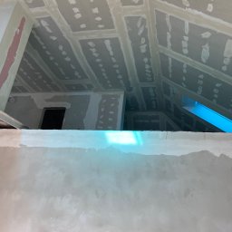 WELL DONE Bartłomiej Paliga - Sufit poddasza po szpachlowaniu, widoczne łączenia płyt gipsowych i otwory po wkrętach wypełnione masą. Ściana w dole kadru pokryta gładzią.