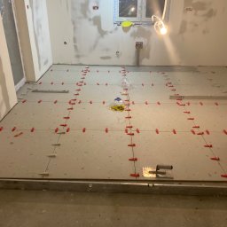 WELL DONE Bartłomiej Paliga - Ułożone płytki podłogowe w trakcie prac wykończeniowych z użyciem poziomicy i klipsów dystansowych. Ściany przygotowane pod malowanie.