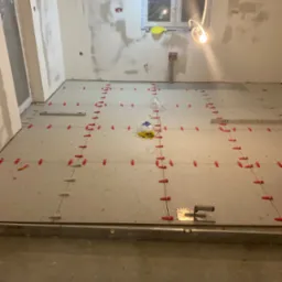 Ułożone płytki podłogowe w trakcie prac wykończeniowych z użyciem poziomicy i klipsów dystansowych. Ściany przygotowane pod malowanie.