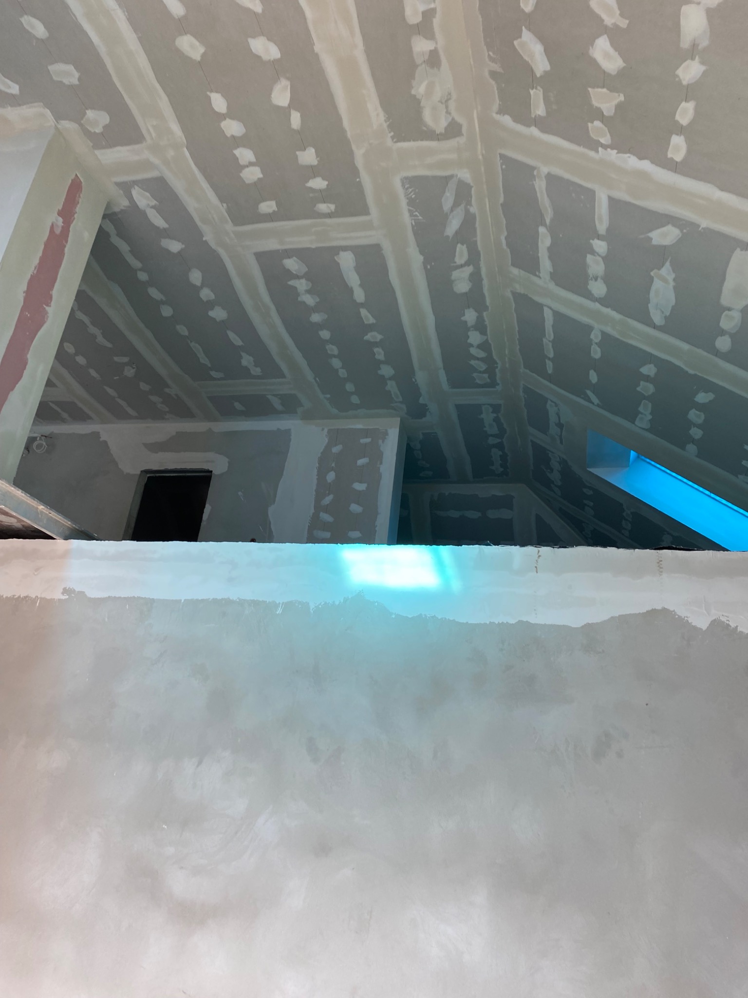 Sufit poddasza po szpachlowaniu, widoczne łączenia płyt gipsowych i otwory po wkrętach wypełnione masą. Ściana w dole kadru pokryta gładzią.