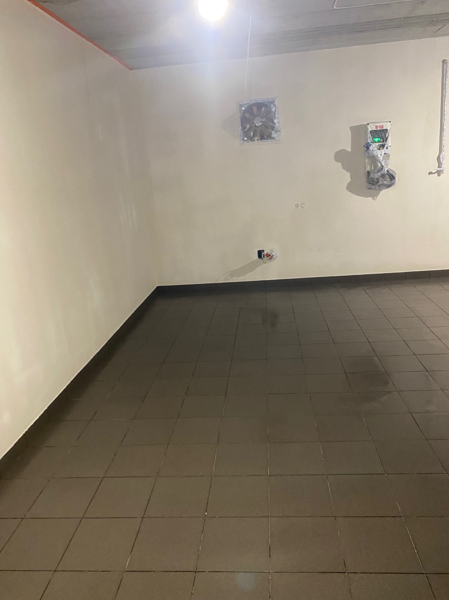 Wykończona łazienka z brązowymi płytkami podłogowymi i beżowymi ścianami. Widoczne elementy instalacji i wentylacji, czekające na podłączenie. Surowy, ale czysty stan.