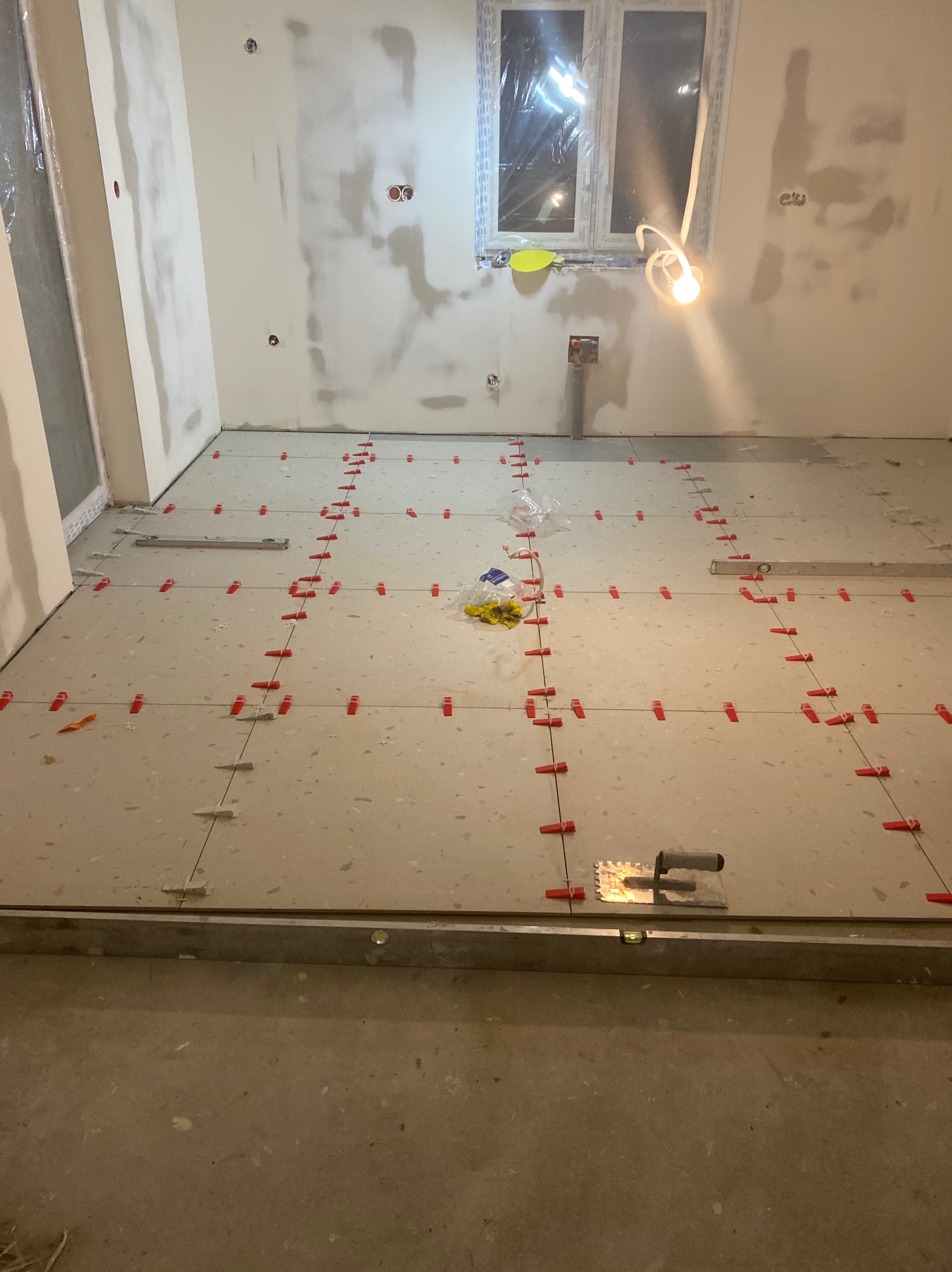 Ułożone płytki podłogowe w trakcie prac wykończeniowych z użyciem poziomicy i klipsów dystansowych. Ściany przygotowane pod malowanie.