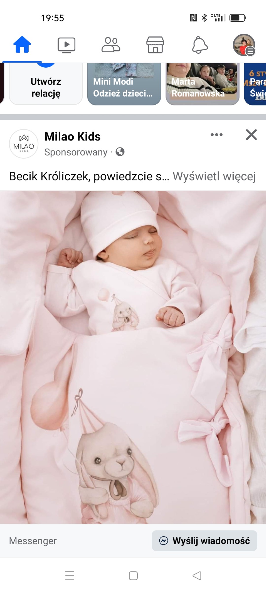 Śpiące niemowlę w jasnoróżkowym beciku z motywem króliczka w czapeczce i balonikiem, ubrane w jasnoróżkowy kombinezon i czapeczkę.
