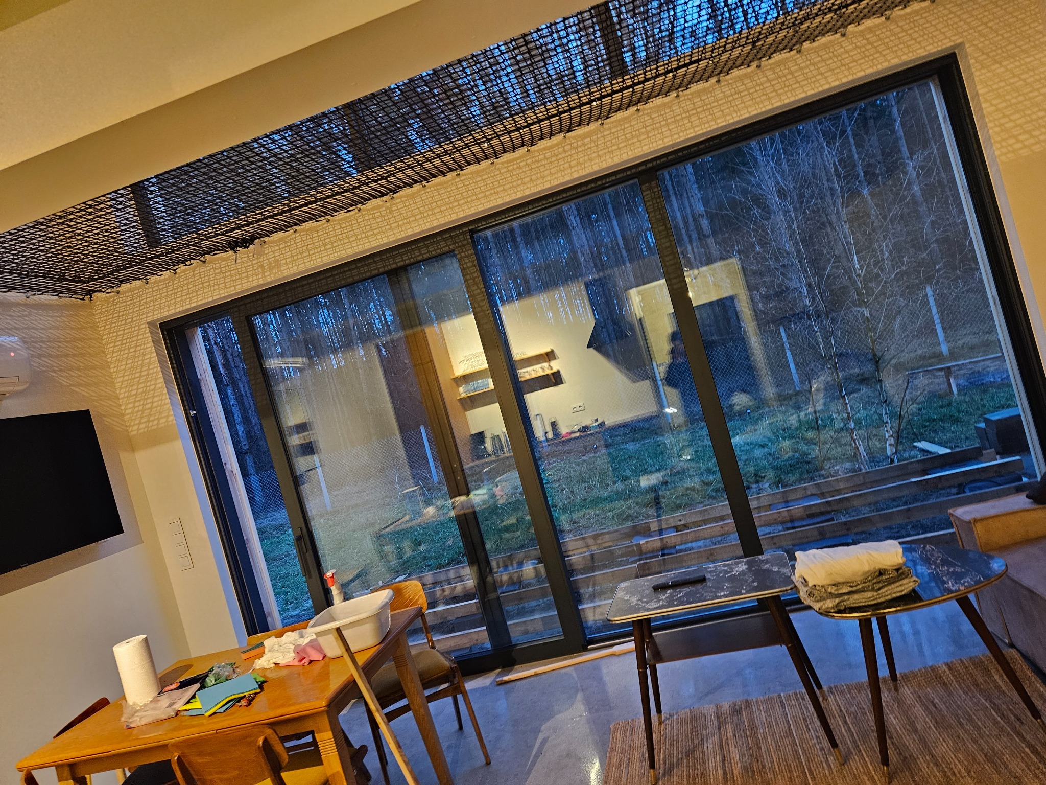 Wnętrze pokoju z dużymi oknami przed myciem: widoczne narzędzia i akcesoria do czyszczenia na stole, w tle krajobraz za oknem.